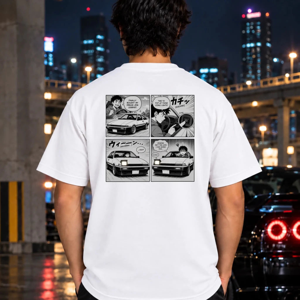 A man viewed from behind wearing a white t-shirt with a black and white comic panel graphic on the back, set against a blurred nighttime city street background with cars.