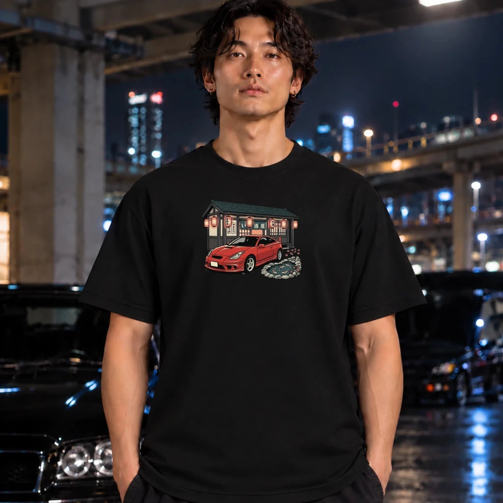 A man wearing a black graphic t-shirt with a red sports car illustration, standing in a city parking structure at night.