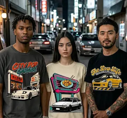 Three young adults standing together on a city street at night, each wearing a graphic T-shirt. The shirt on the left is dark gray with a colorful 'City Pop Garage' graphic and a white car illustration.